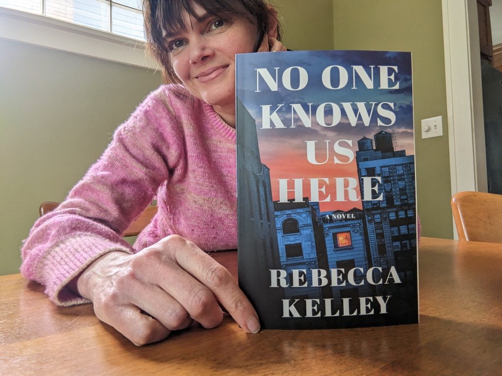 Rebecca Kelley sitting at the table with a copy of No One Knows Us Here